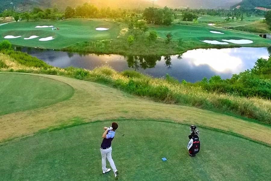 Golfer teeing off above a lake on a golf course in Central Vietnam